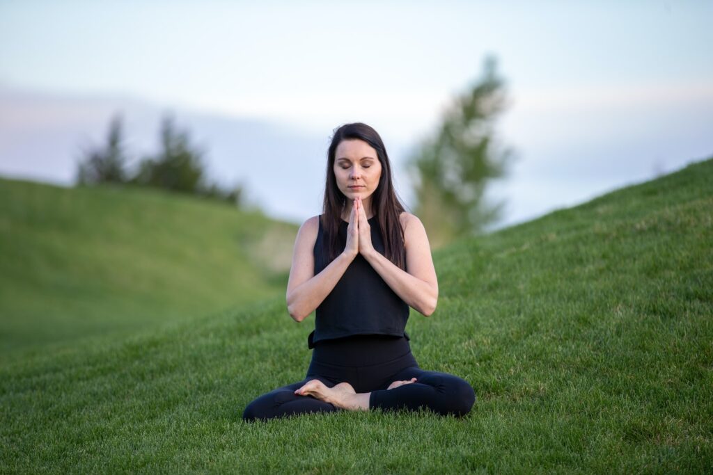 meditatie woman in black tank top and black pants sitting on green grass field during daytime