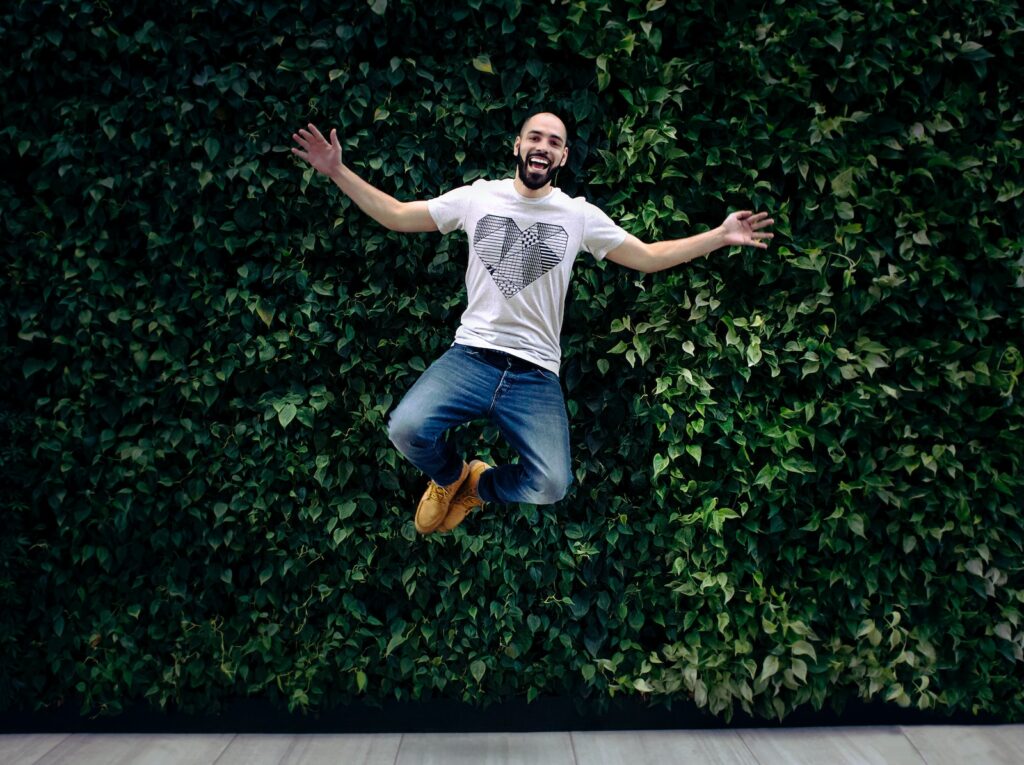 meditatie man wearing t-shirt and jeans jumpshot in front of a green hedge